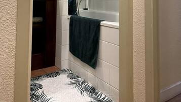 A bathroom with a bathtub, a shower, and a toilet. There is a towel hanging on the wall and a patterned mat on the floor.