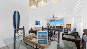 A modern living room with a glass coffee table, wicker side table, and a 'Welcome' sign. - Harbor Cottage North Coast Village G36-Ocean Views-*Super Close To Beach* (Oceanside)