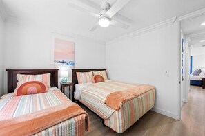 Un dormitorio con dos camas, ventilador de techo y mesita de noche con lámpara.