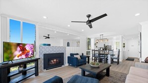 A modern living room with a fireplace, a TV, and a dining area with chairs and a table. - Harbor Cottage North Coast Village G36-Ocean Views-*Super Close To Beach* (Oceanside)