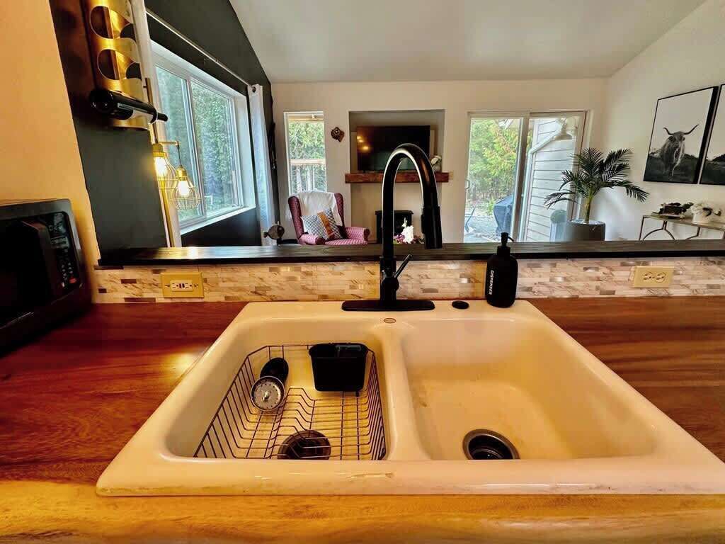 Eine Küche mit doppelter Spüle, Holz Arbeitsplatten, einem eingebauten Ofen und einem Fenster mit Blick auf eine Terrasse.