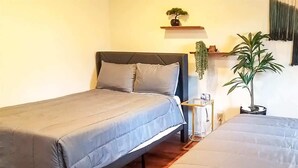 Ein Schlafzimmer mit zwei Betten, einem Nachttisch, einer Lampe und einer Zimmerpflanze.