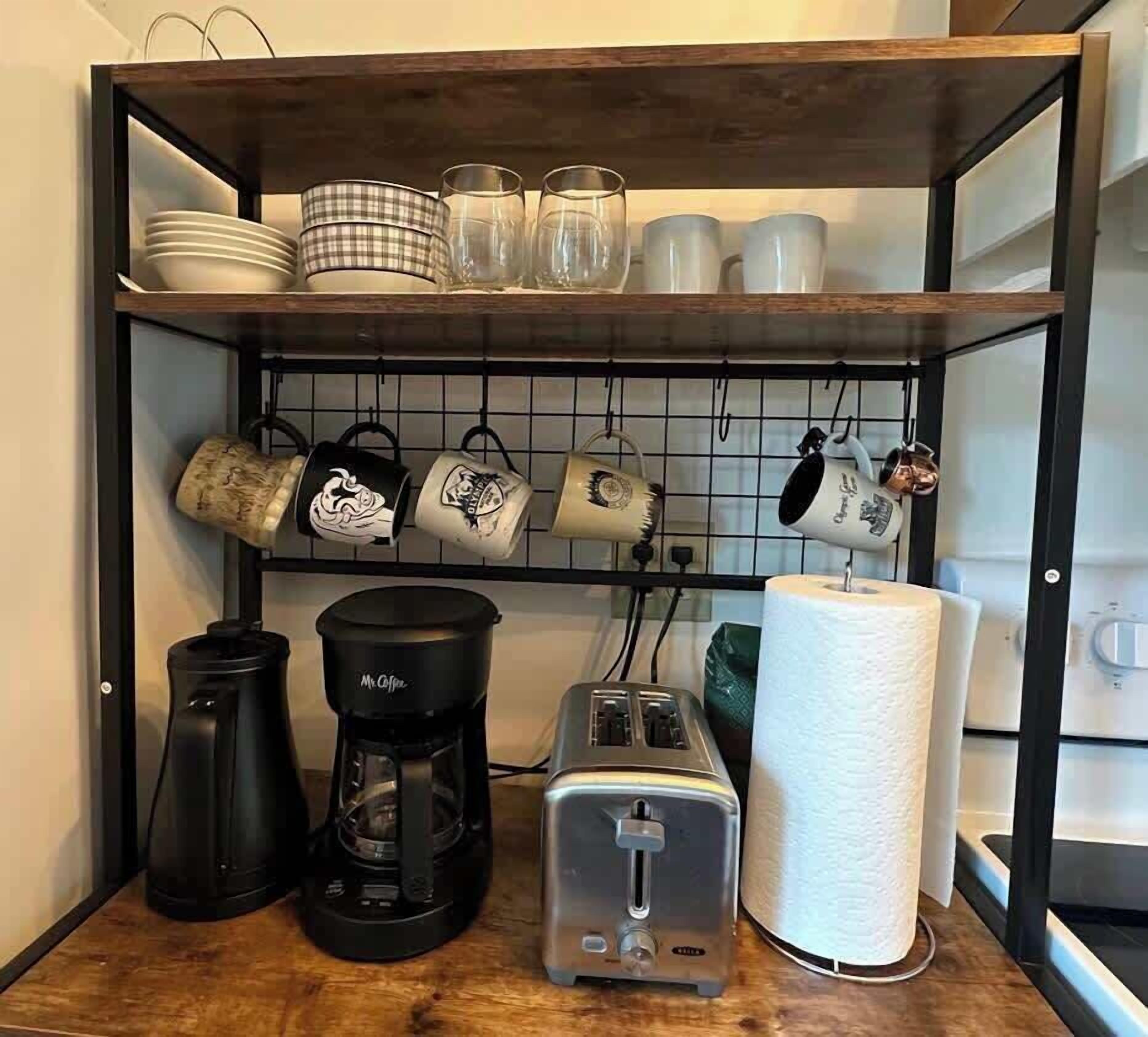 A kitchen area with a coffee maker, toaster, and hanging mugs on a shelf.