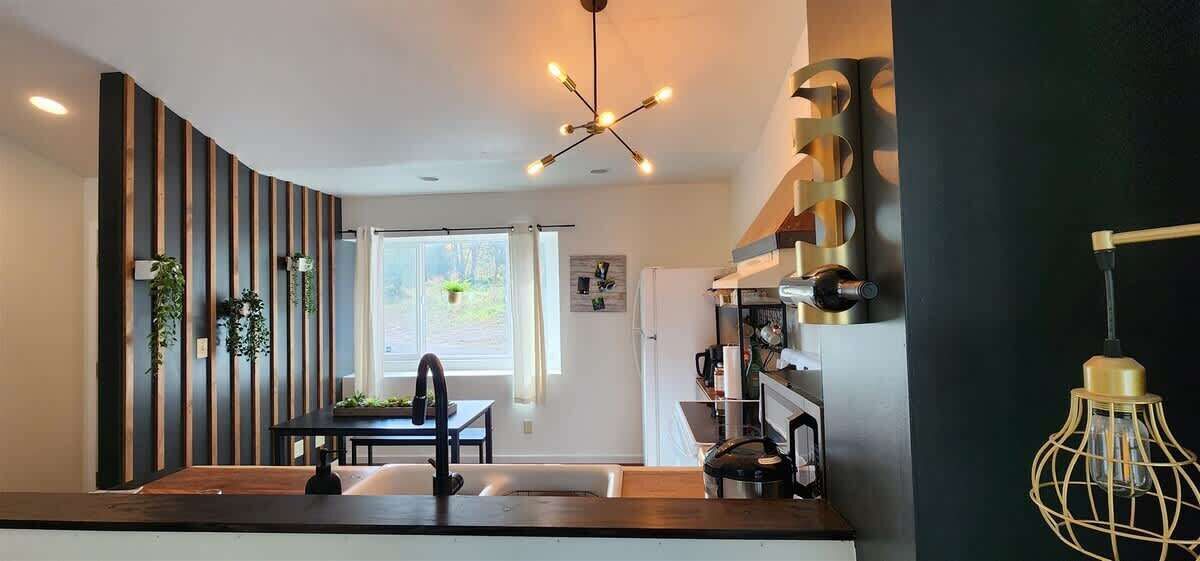 Een moderne keuken met een centraal eiland, een eetgedeelte met tafel en stoelen, en een uitzicht op de omgeving door een groot raam.