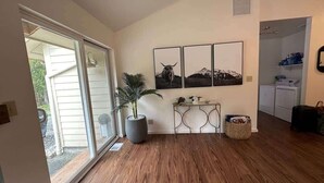 Une pièce dotée d’un plancher en bois, d’une plante en pot, d’une console ornée d’objets décoratifs et d’un tableau représentant un paysage de montagne accroché au mur.