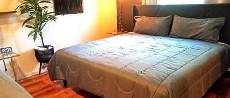 A hotel room with a bed, a bedside table, a lamp, a potted plant, and a wall clock.