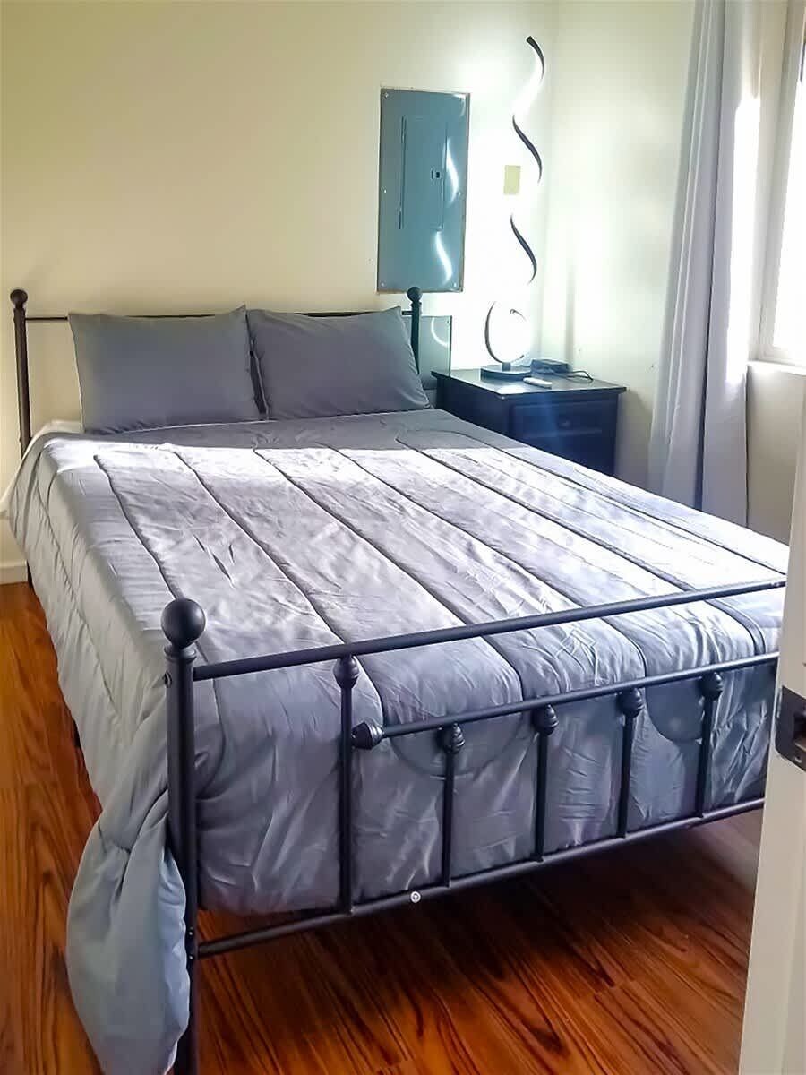 Un lit avec un cadre en métal, un plancher en bois, une table de chevet et une lampe fixée au mur.