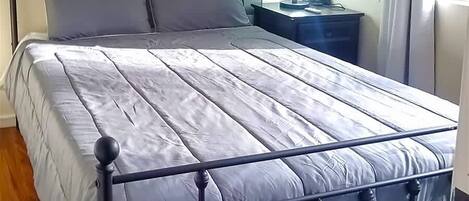 Un lit avec un cadre en métal, un plancher en bois, une table de chevet et une lampe fixée au mur.