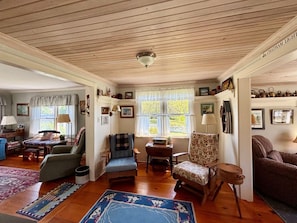 A cozy living room with wooden floors, a fireplace, and a variety of seating options including a sofa, chairs, and a rug.