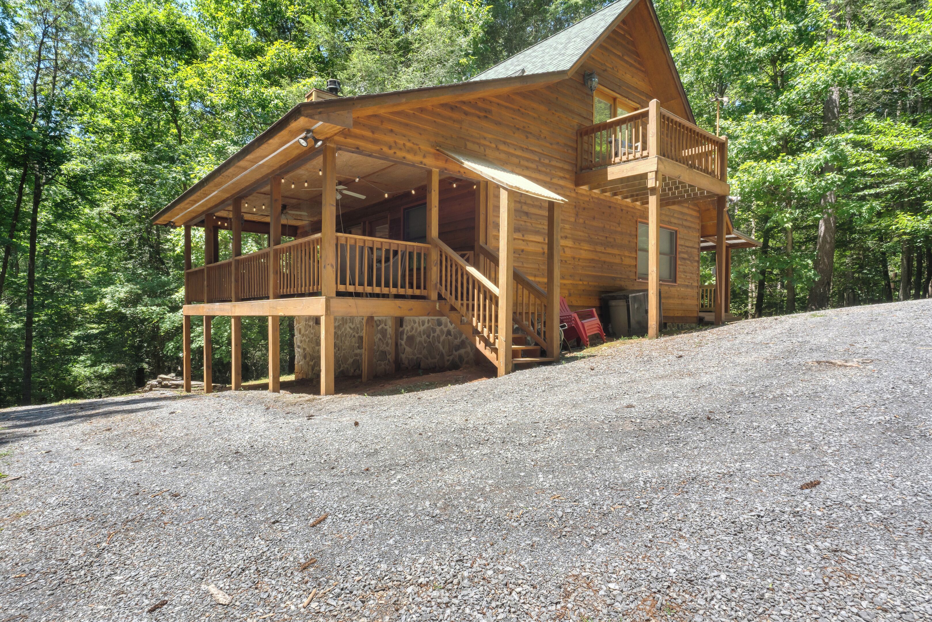A wooden cabin with a porch and a balcony, surrounded by trees.