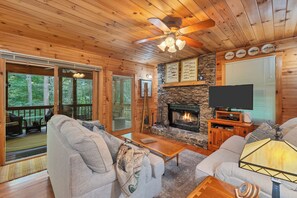 A cozy cabin interior with a stone fireplace, wooden ceiling, and a television on a wooden stand.