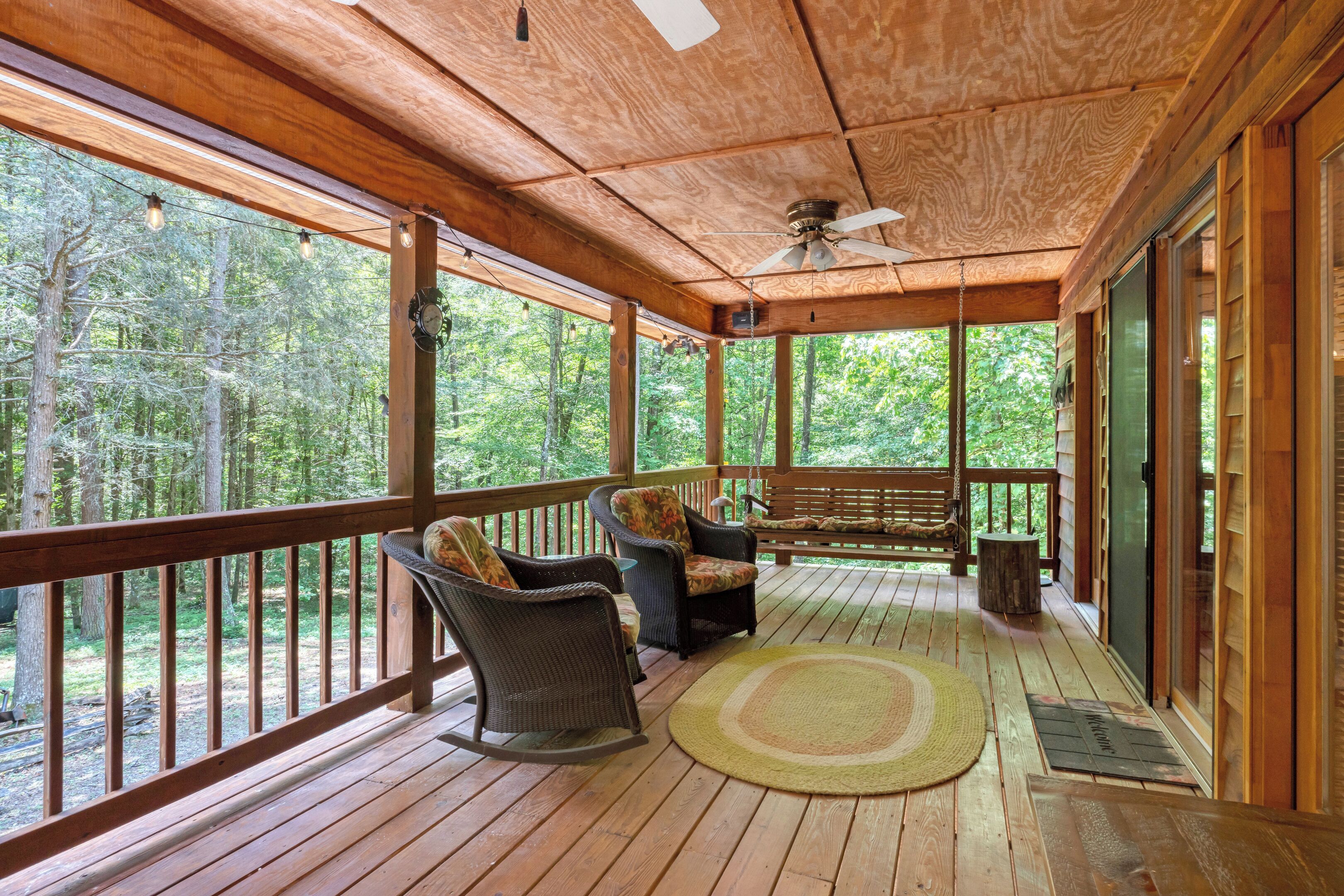 A wooden deck with wicker chairs and a bench, overlooking a forested area.