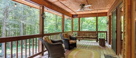 A wooden deck with wicker chairs and a bench, overlooking a forested area.