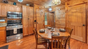 A wooden-paneled kitchen with a stainless steel stove, wooden cabinets, and a round dining table set for four. - SECLUDED♤Bonfire pit♤2 bdrm/2bath♤Pet friendly (Townsend)