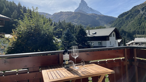 A wooden table with a bottle and a wine glass on a balcony overlooking a mountain with a distinctive peak. - Studio with magnificiant view of the Matterhorn (Zermatt)