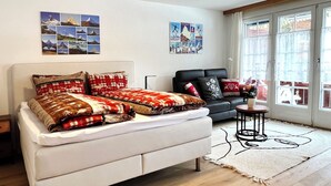 A modern living room with a white sofa, a black armchair, and a small side table. There are wall art pieces and a large window with curtains. - Studio with magnificiant view of the Matterhorn (Zermatt)