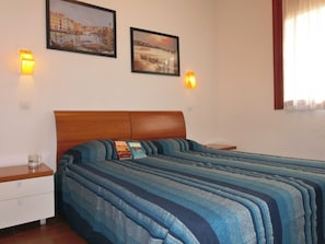 Un dormitorio con una cama, dos mesitas de noche, una mesilla auxiliar, dos lámparas de pared y dos cuadros enmarcados.