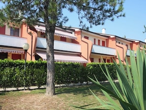 Un edificio con fachada roja y blanca, un árbol en primer plano y un seto bien cuidado.