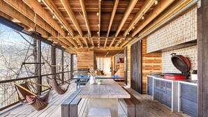 A spacious wooden deck with a central table, hanging hammocks, and a grill area. - Architect designed w/ Sauna, Hot Tub, Fire Pit, Swings, Game Rm,3 near Asheville (Mars Hill)
