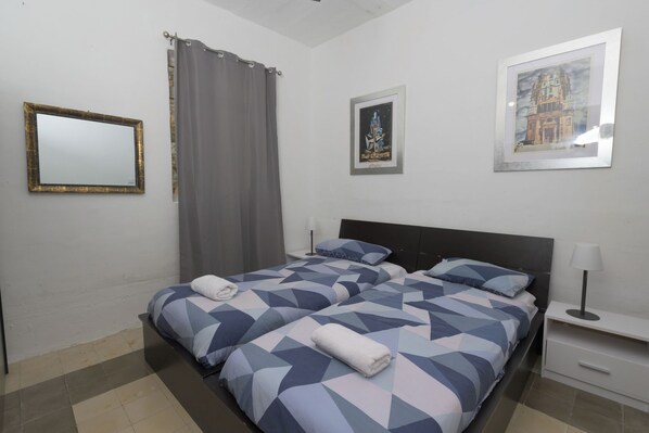 A hotel room with a bed, a nightstand, a lamp, a mirror, and two framed pictures on the wall.