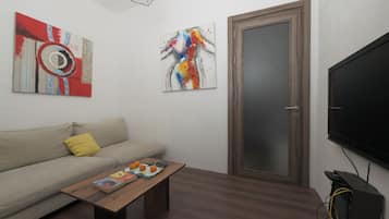 A living room with a sofa, coffee table, artwork, door, and a TV.