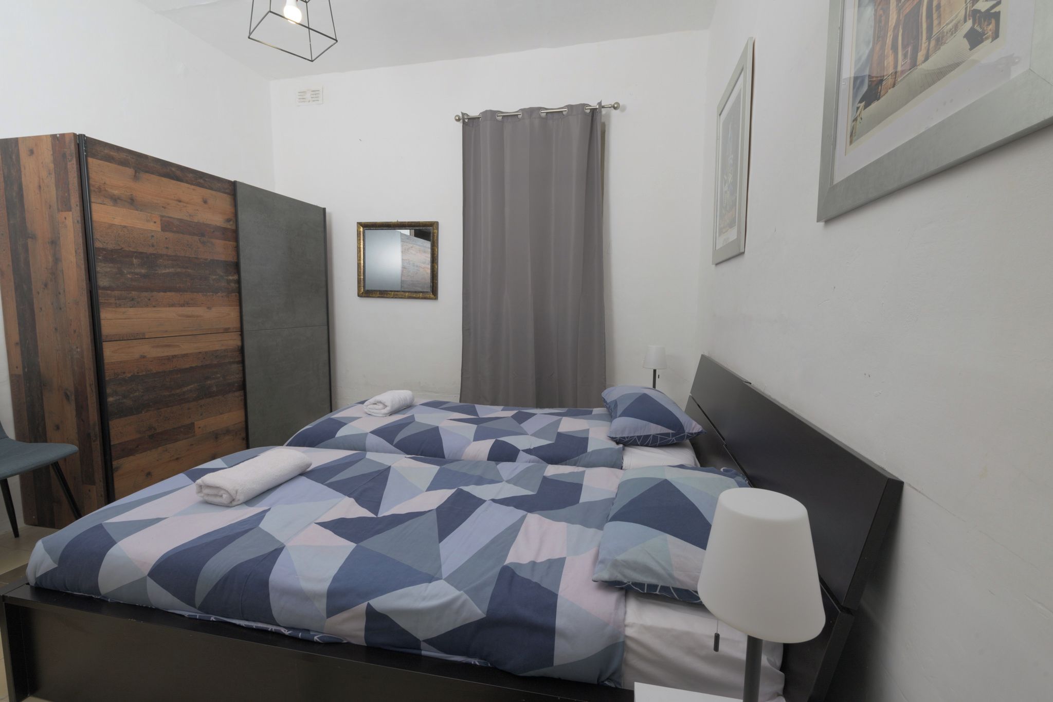 A modern bedroom with a bed, a nightstand, a lamp, a wardrobe, and a window with curtains.