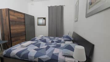 A modern bedroom with a bed, a nightstand, a lamp, a wardrobe, and a window with curtains.