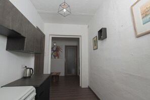 A narrow hallway with a kitchen area on one side, a door at the end, and a framed picture on the wall.