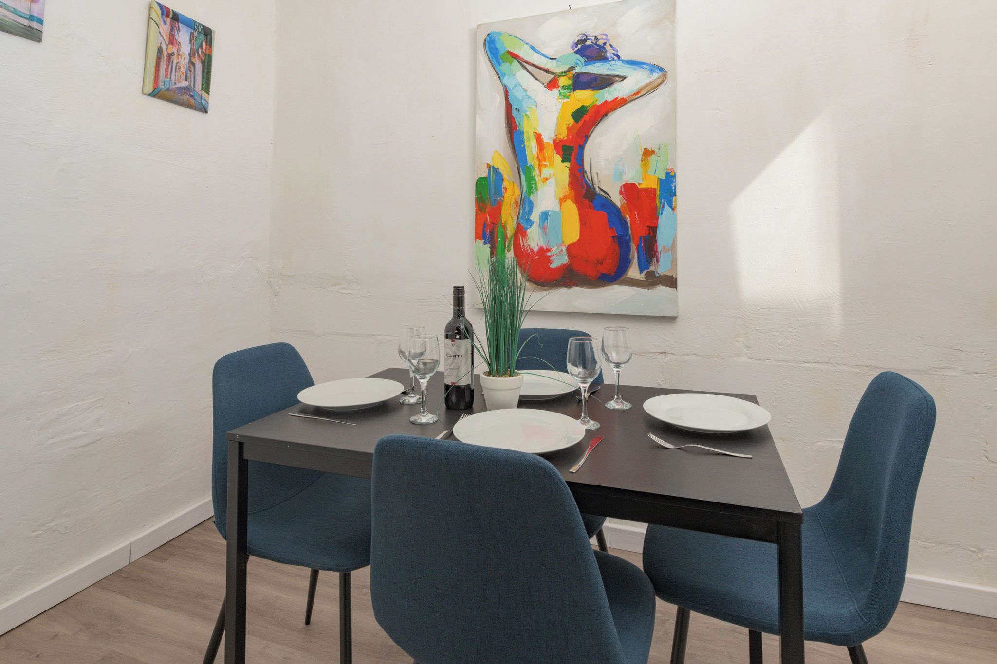 A dining area with a table set for four, chairs, a wine bottle, and a potted plant.