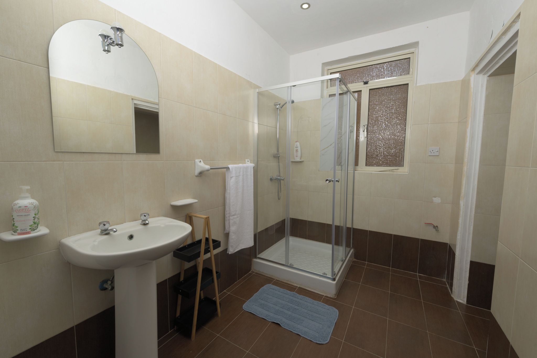 A bathroom with a sink, mirror, shower, and a towel rack.