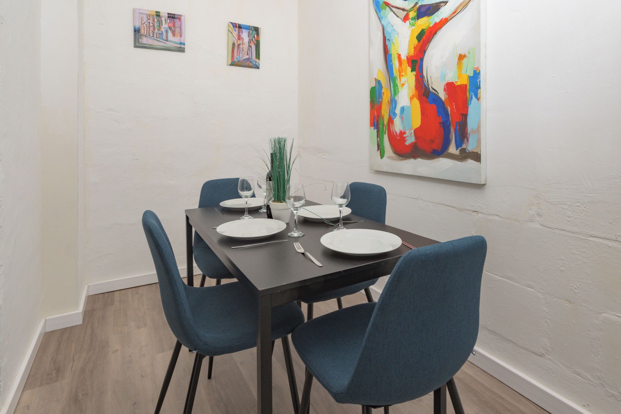 A dining area with a rectangular table set for four, surrounded by blue chairs, with a potted plant on the table.