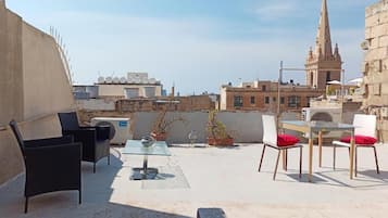 Una terrazza sul tetto con mobili da esterno, piante in vaso e vista sulla città, con la guglia di una chiesa.