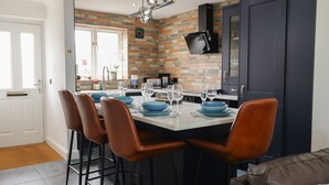 A modern kitchen with a brick wall backsplash, a dark blue cabinet, and a bar area with stools. - Tritons Retreat (Moelfre)