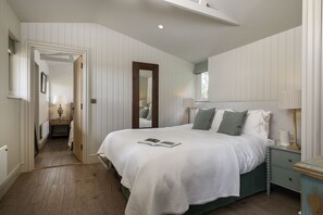 A bedroom with a bed, bedside tables, a mirror, and a door leading to another room.