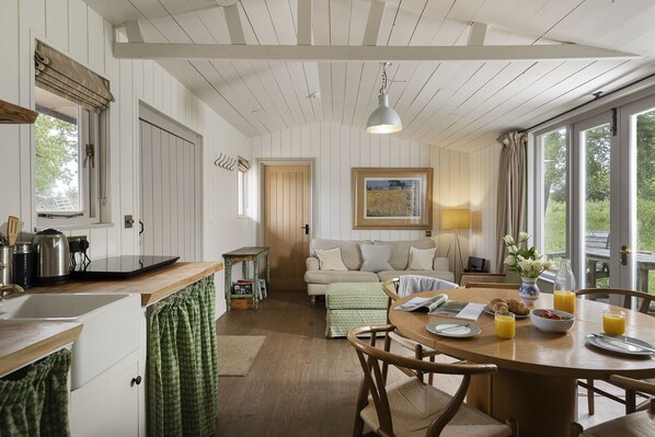 A cozy kitchen with wooden cabinets, a dining table with chairs, a sofa, and a window with a view of greenery.