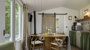 A dining area with a wooden table and chairs, a television mounted on the wall, and a kitchen area with a microwave and utensils. - Dog friendly holiday home with a hot tub and woodland views - Keepers Stable (Cranham)