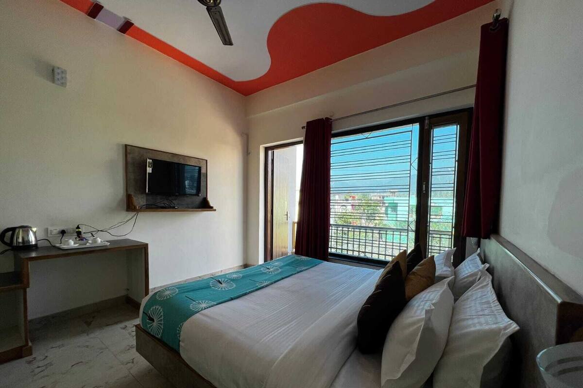 Ein Hotelzimmer mit einem Bett, einem an der Wand montierten Fernseher, einem Schreibtisch mit Wasserkocher und einem mit Vorhängen versehenen Fenster.