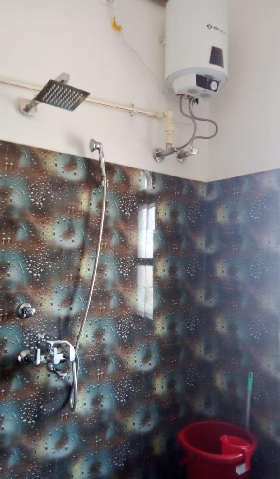 A bathroom with a shower, a red bucket, and a wall-mounted air conditioner.