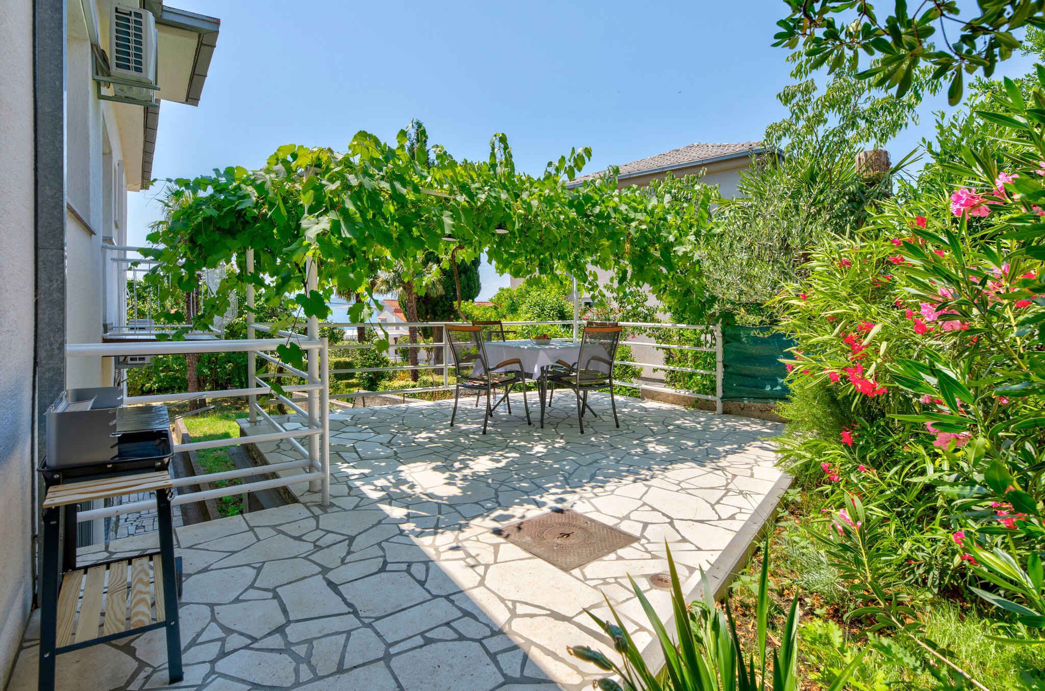 A patio with a stone floor, a table and chairs, and a pergola with vines.