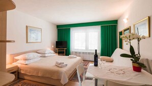 Habitación de hotel con cama, una mesa con botella y vaso, televisión y planta.