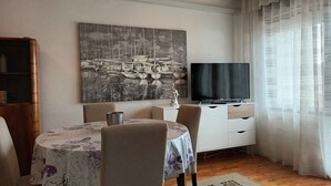 A dining area with a round table, chairs, a television, and a painting on the wall. - Holiday apartment with terrace and air conditioning (Selce)