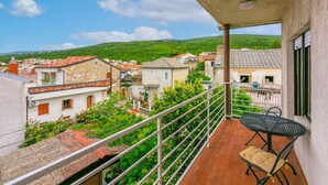 A balcony with a table and chair, overlooking a residential area with stone buildings and greenery. - Holiday apartment with terrace and air conditioning (Selce)