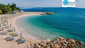 A beach with rows of sun loungers and umbrellas, a rocky shoreline, and a clear blue sea. - Holiday apartment with terrace and air conditioning (Selce)