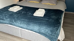 A neatly made bed with a blue patterned bedspread and two pillows, a wall with a blue accent and a circular decoration with branches and butterflies, and a bedside table with a lamp.
