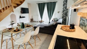 A modern kitchen with a central island, a dining area with a glass table, and a staircase leading to an upper level.