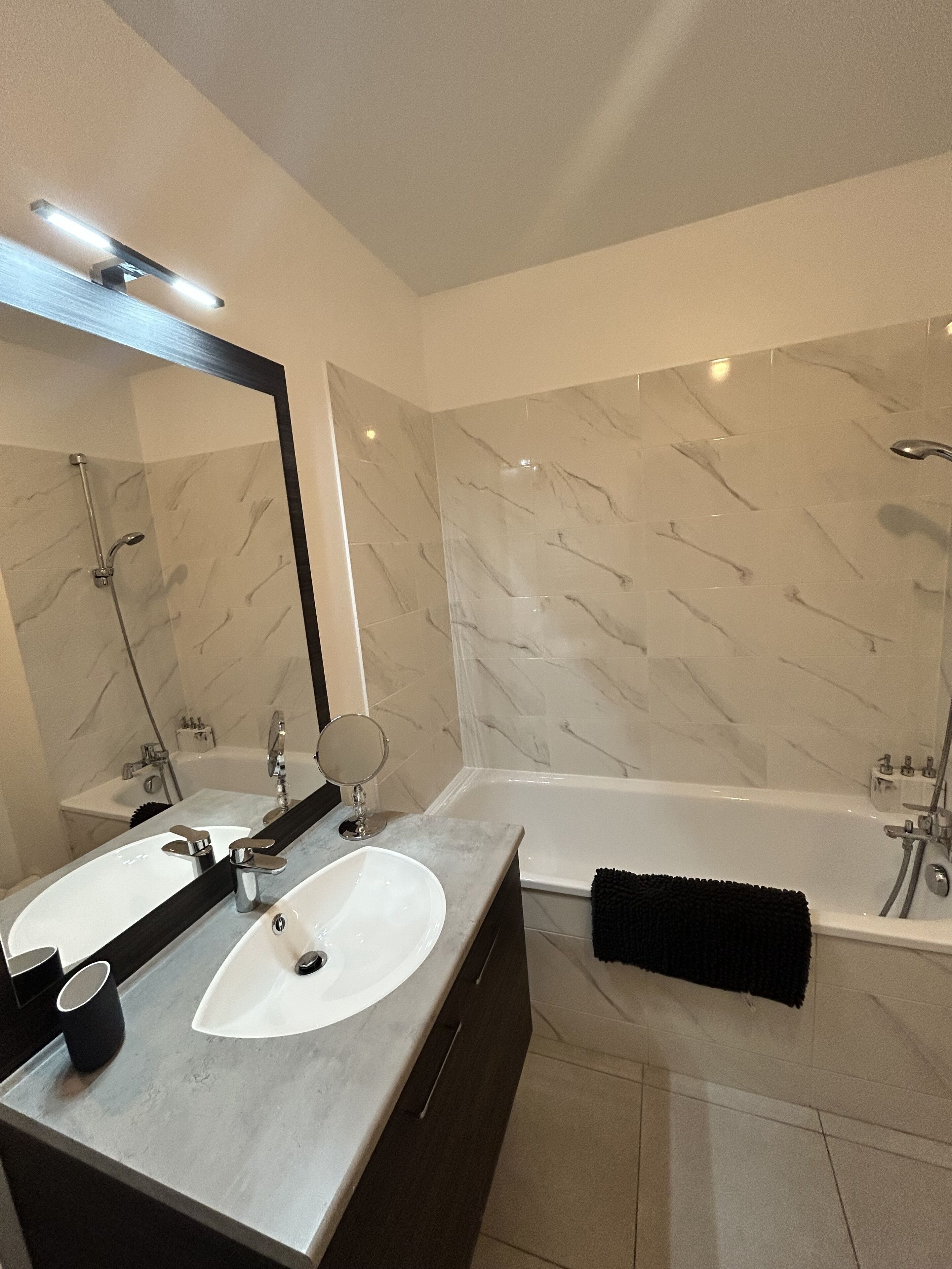 Une salle de bain moderne avec deux lavabos, un grand miroir et une baignoire.