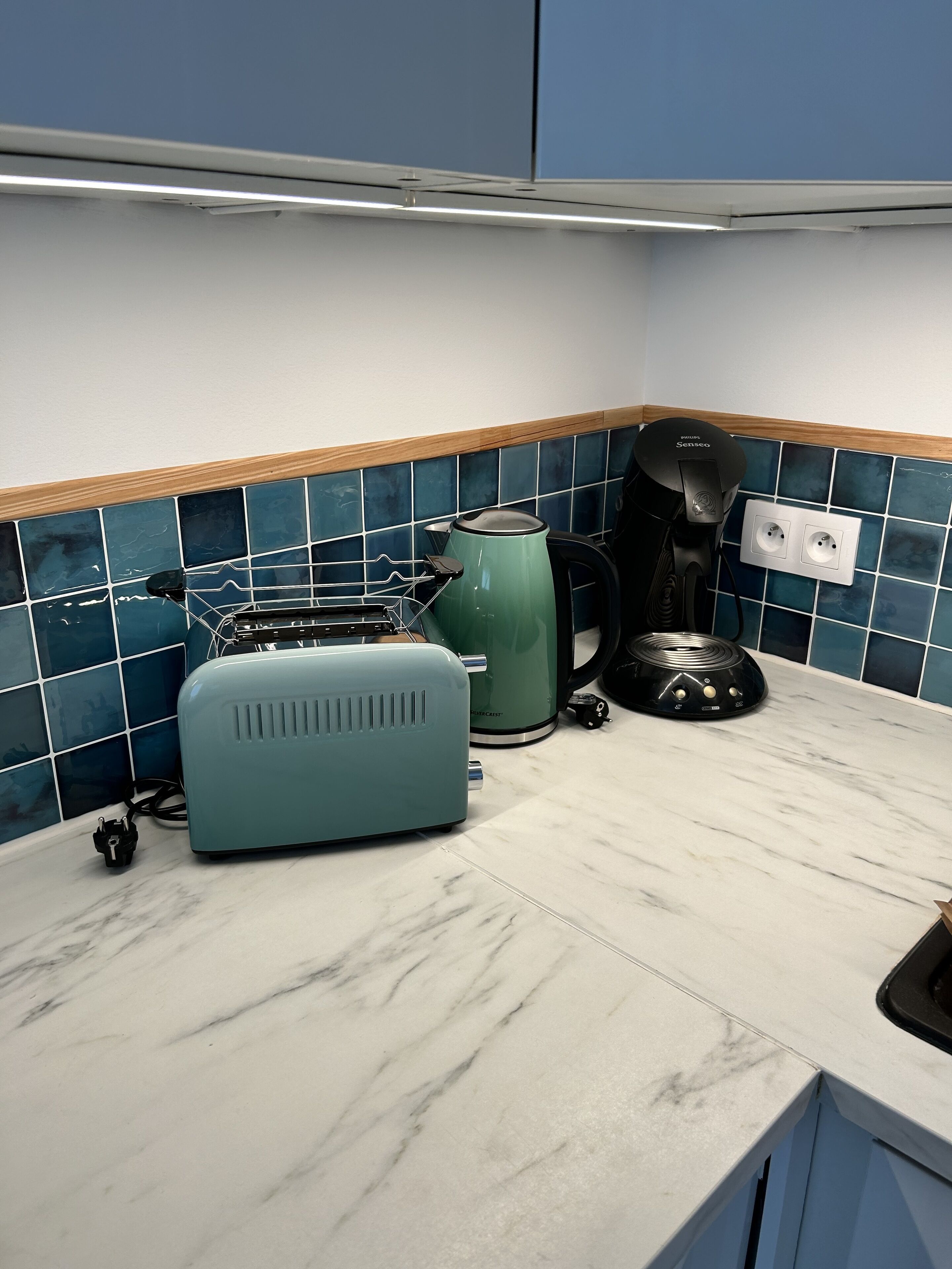 A kitchen with a marble countertop, a toaster, a kettle, and a coffee maker.