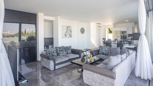 A modern living room with grey sofas, a glass coffee table, and a view of the city through large windows. - Villa Aria, Luxury 3BDR Protaras Villa with Private Pool, Close to the Beach (Protaras)