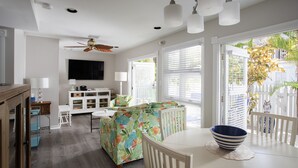 A bright living room with a ceiling fan, a TV, and a dining area with a table and chairs. - Shipyard 208-6 Condo in Truman Annex-2 bedroom 2 bath, close to Duval w/ pool (Key West)