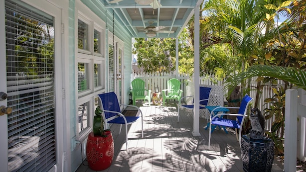 A covered porch with blue and white chairs, a red pot, and a ceiling fan. - Shipyard 208-6 Condo in Truman Annex-2 bedroom 2 bath, close to Duval w/ pool (Key West)